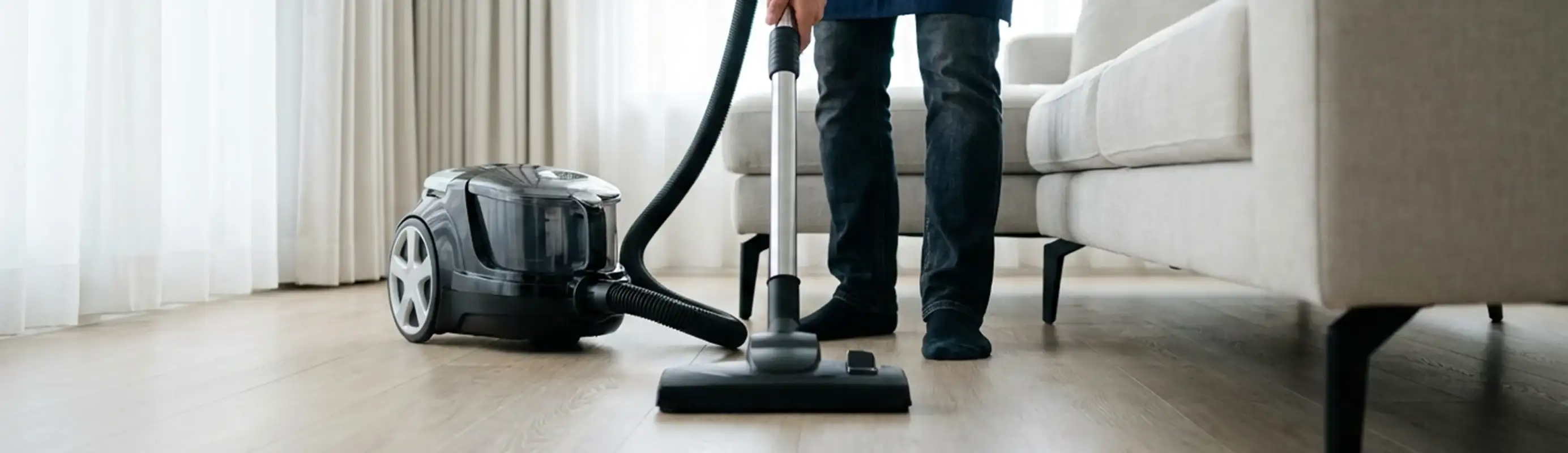 Professional house cleaner vacuuming a living room floor with a canister vacuum cleaner, Bakersfield, CA.