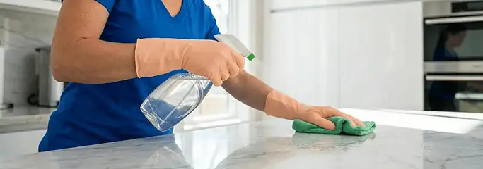 Maid service worker spraying and wiping a kitchen countertop with a microfiber cloth for sanitizing, Bakersfield, CA.