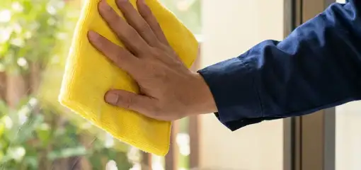 House cleaner wiping a glass window with a yellow microfiber cloth for streak-free cleaning, Bakersfield, CA.